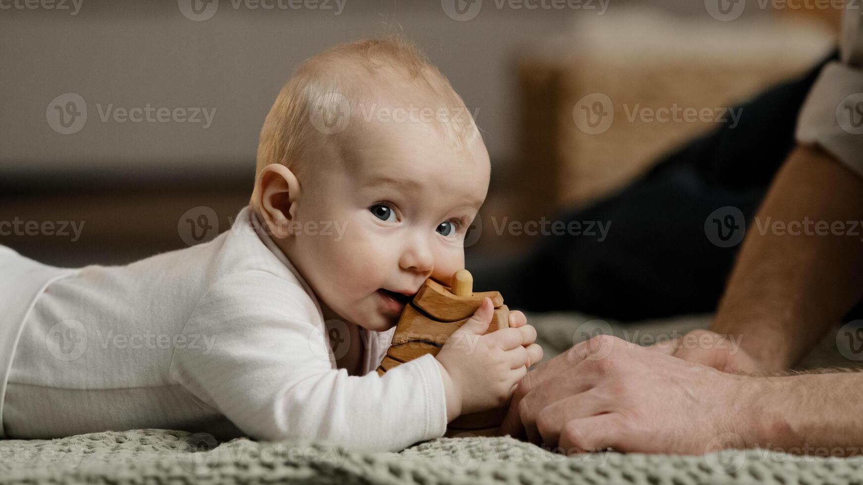 Caucasian family unrecognizable father daddy play with little daughter son infant newborn toddler lying at home on floor with toys baby bites wooden constructor teething concept, man stroking head photo