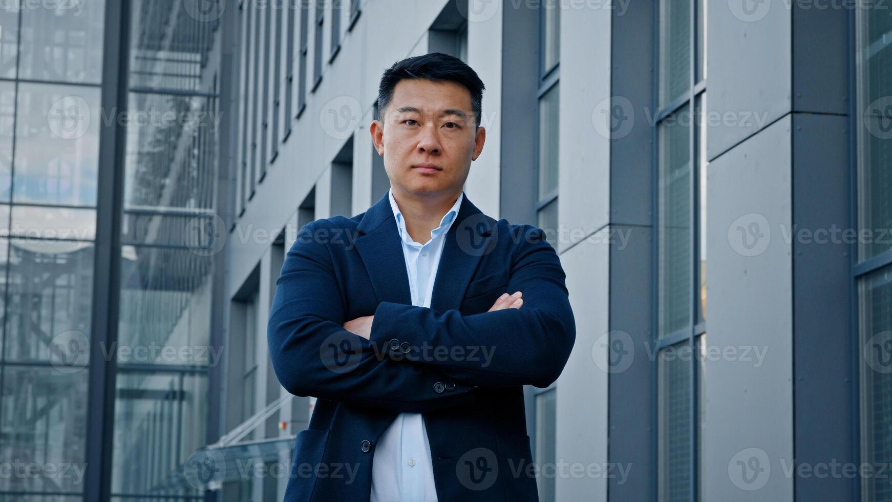 Portrait confident strong pose motivated successful 40s Asian man trader entrepreneur businessman boss leader employer crossing hands posing near company office building standing with crossed arms photo