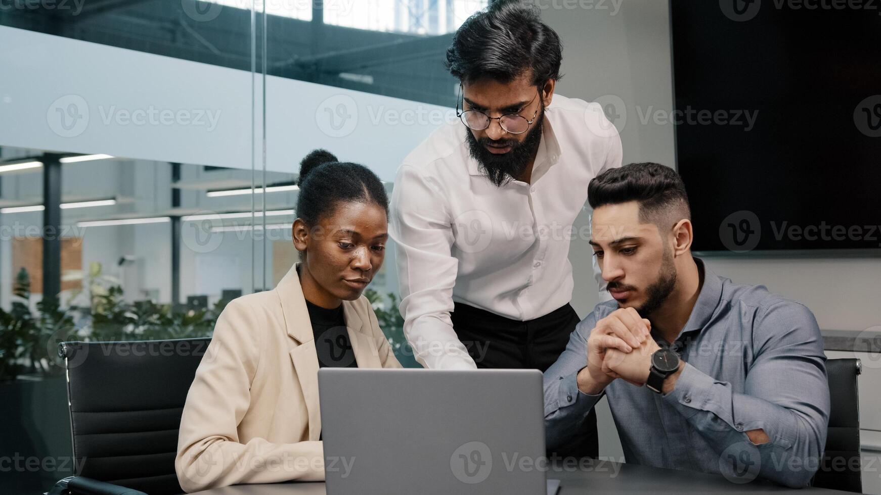 Arab man coach leader boss talking about mistake explain Indian teacher mentor teaching interns managers employees use online app help with software diverse team looking laptop discussing project photo
