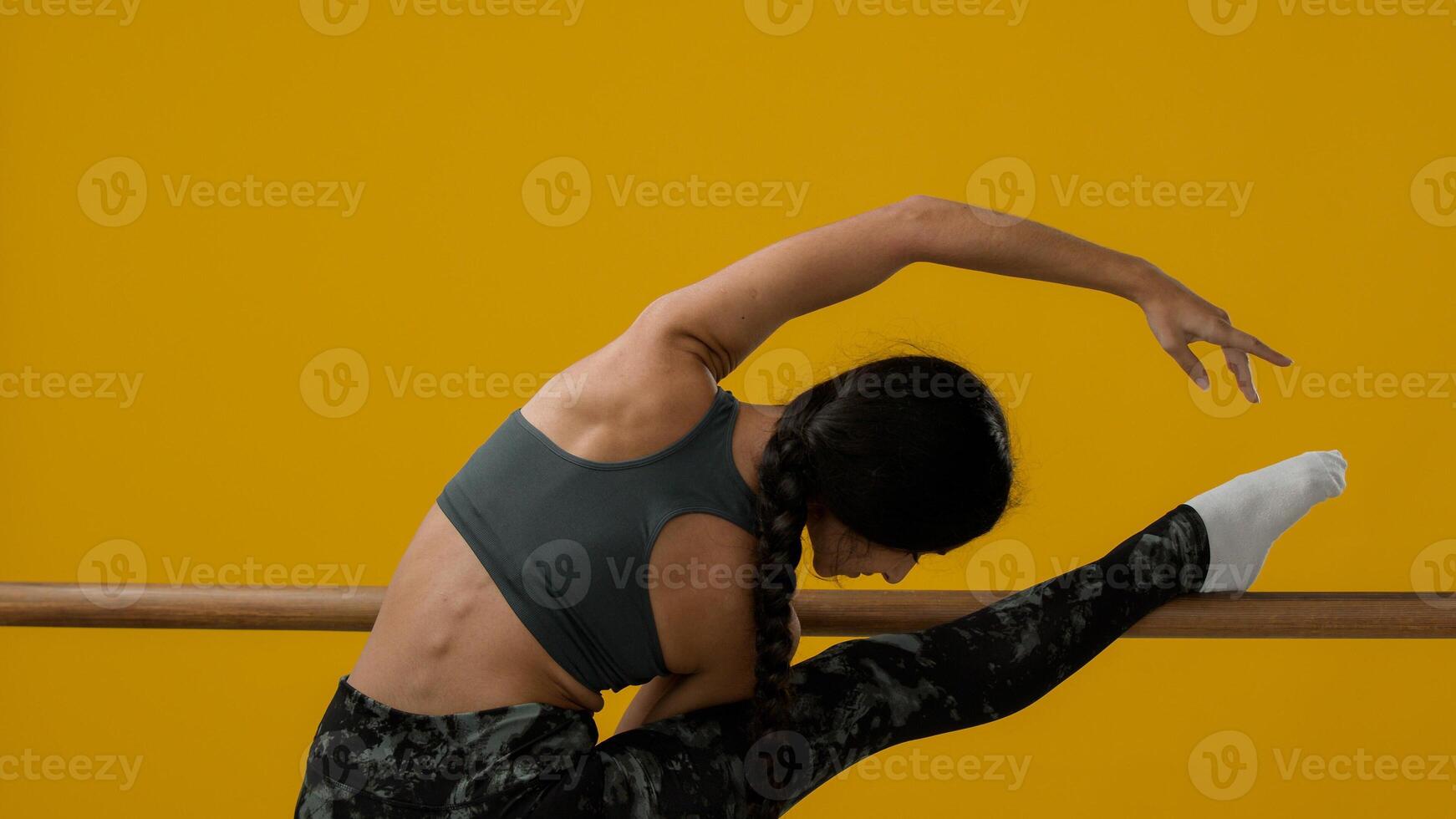Back view from behind flexible graceful Indian slim sporty woman ethnic girl athlete female dancer ballerina lady in yellow studio stretching with ballet barre stretch leg flexible dancing exercise photo