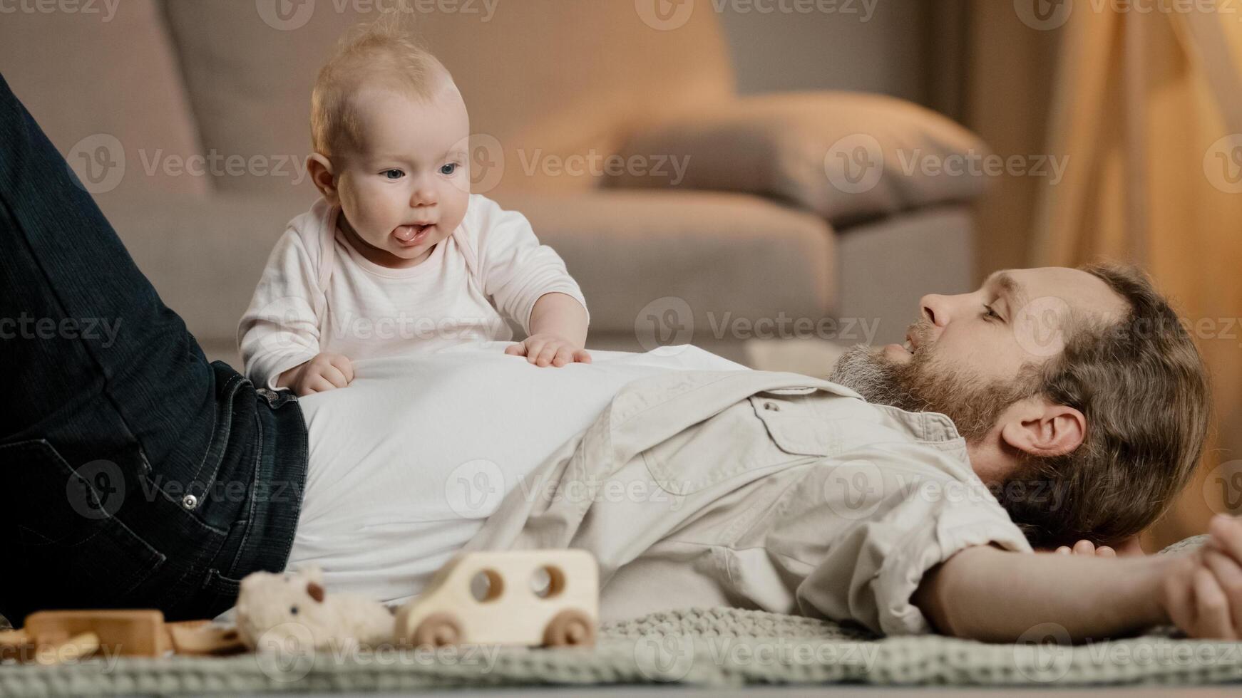 Caucasian family father with little daughter son lie on floor at home play. Baby girl boy newborn kid crawling over daddy child care fatherhood nursery indoors. Children parenthood childhood love photo