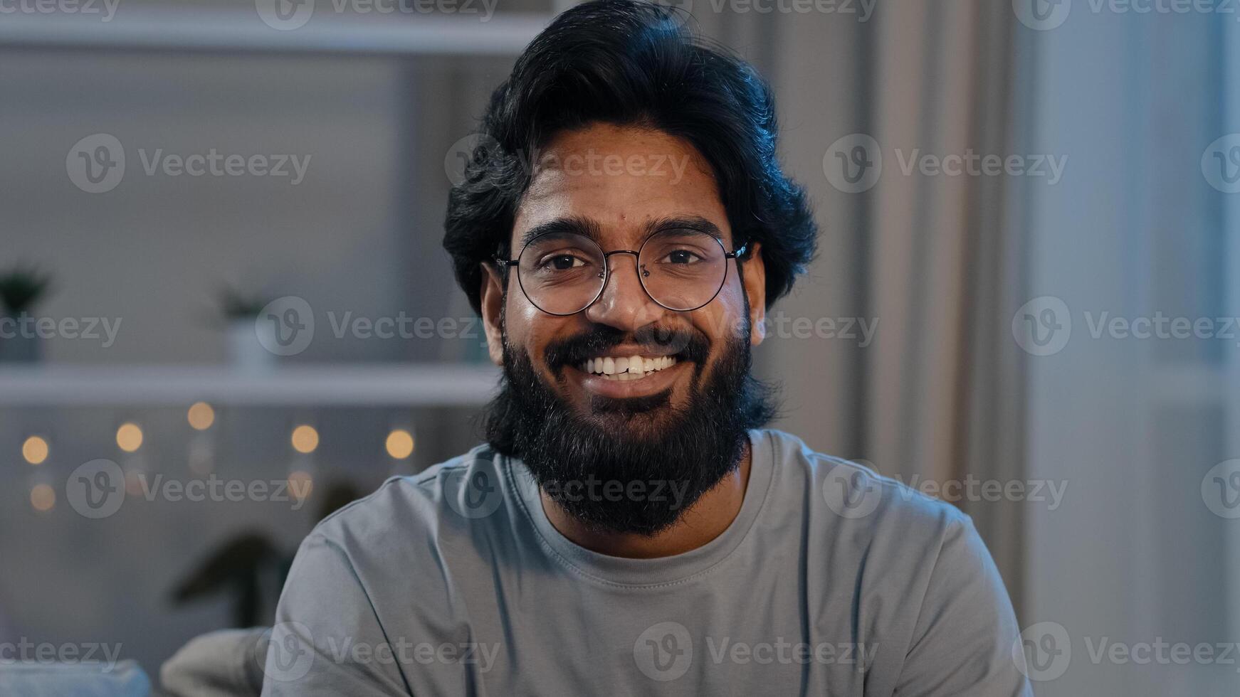 Smiling adult 30s indian arabian bearded man vlogger looking at camera talk make live conference call online chat streaming recording blog vlog at home distant conversation close up webcam view photo