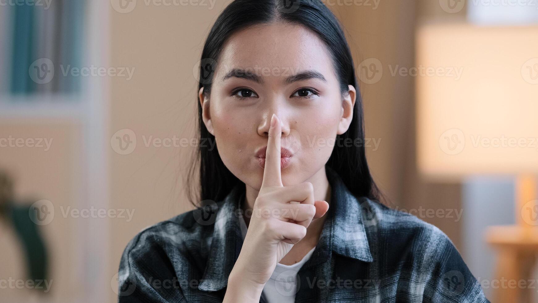 Portrait asian ethnic korean woman point with finger near mouth Chinese Japanese girl makes hush quiet gesture showing secret sign asks silent confidential secrecy information looking at camera indoor photo