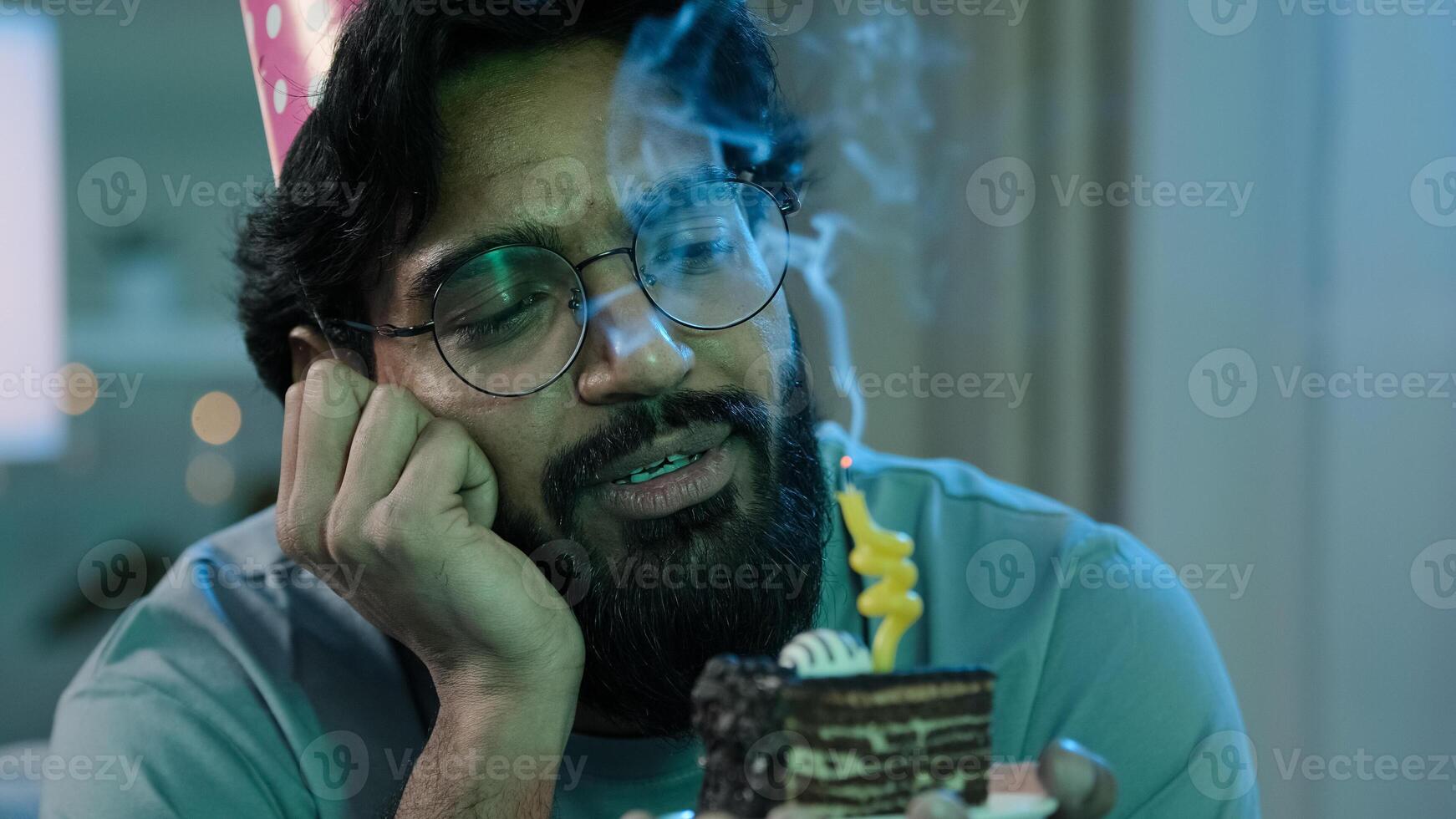 Headshot arabian alone single sad upset lonely bearded man in birthday pink hat and glasses sitting at home at night feel frustrated despair disappointed sadness holds cake with candle photo