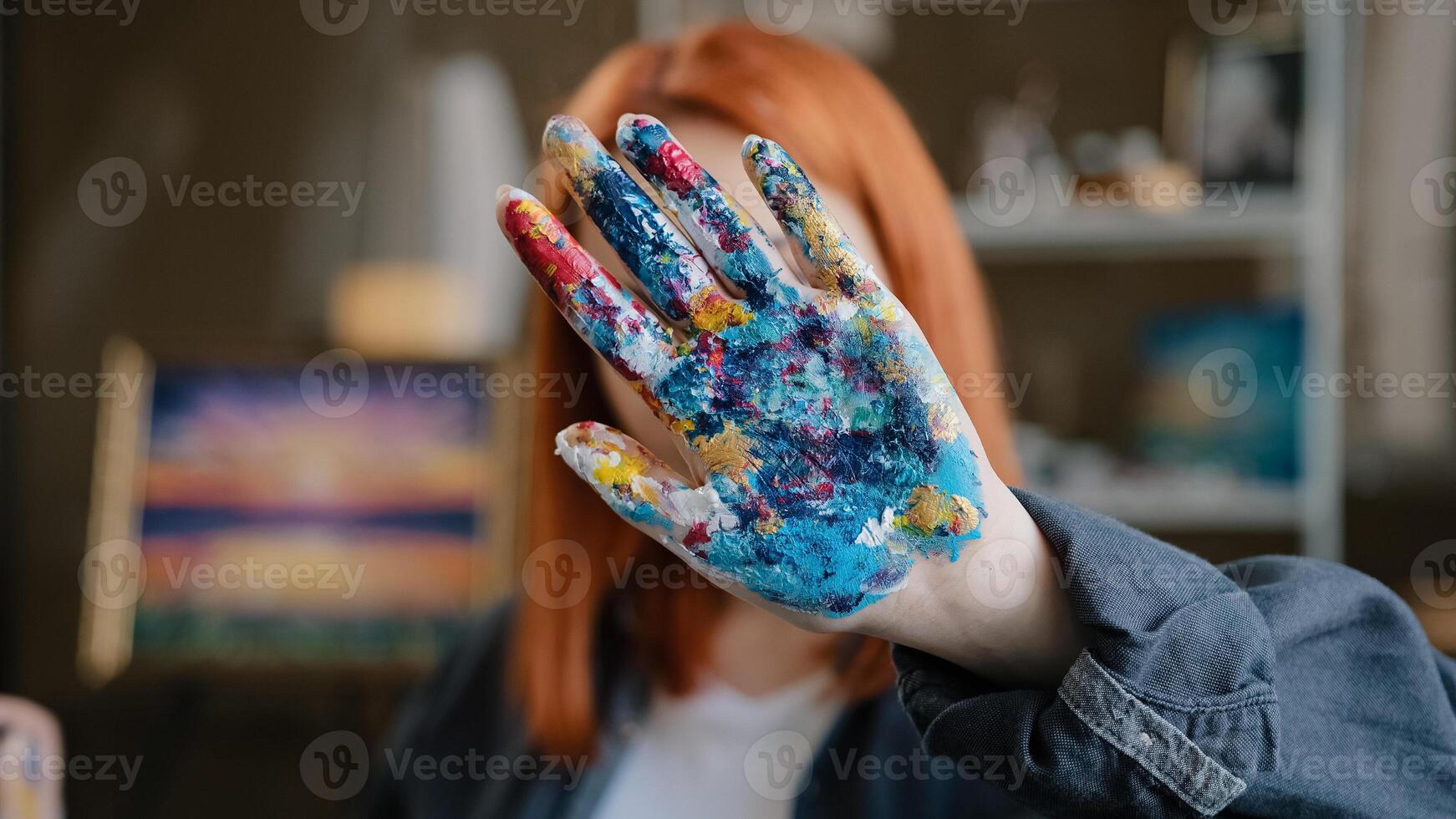 Female calm red-haired girl artist lady Caucasian 30s woman painter designer holding hand in front stop gesture not no gesture showing dirty in acrylic paint palms looking at camera in art studio photo
