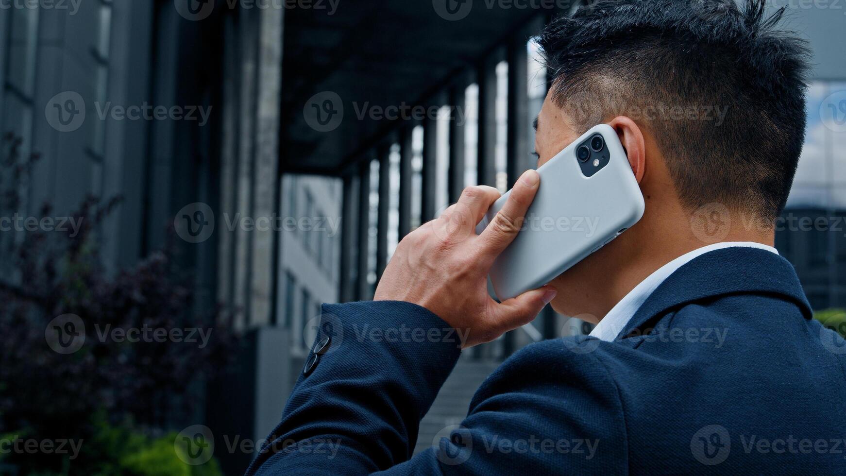 Back view middle-aged Asian businessman CEO employer entrepreneur boss manager formal man has conversation mobile call with phone smartphone communication remote distant talk virtual speaking in city photo