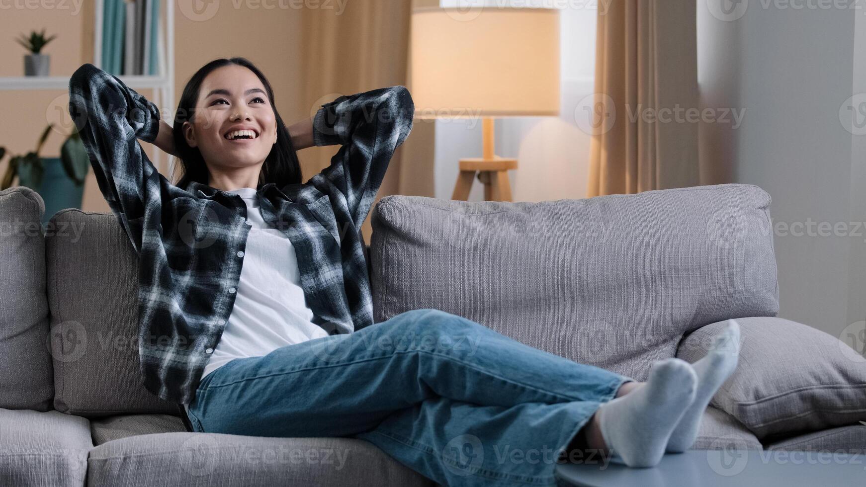 Calm happy tired asian woman housewife resting on soft couch holding hands behind head korean lady relaxing on comfortable sofa napping feel stress free at home lounge peaceful resting indoors cozy photo