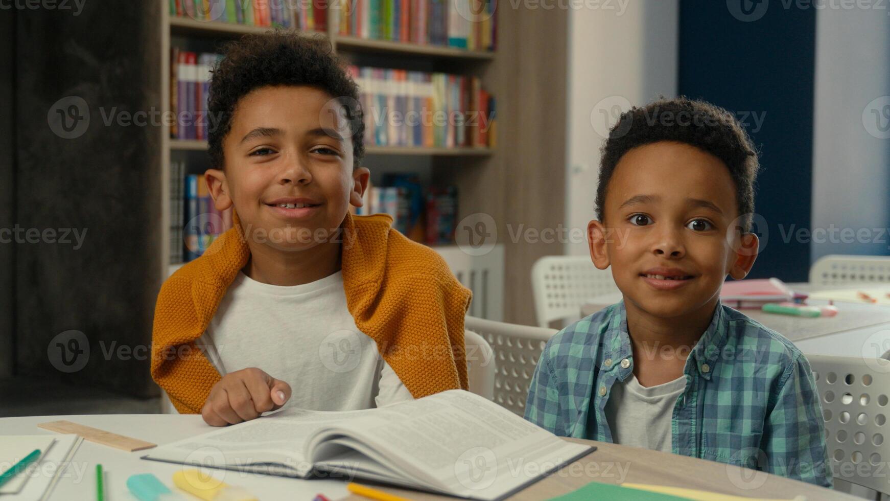 Smiling cute children African American kids brothers siblings friends schoolboys primary school education pupils students little boys at desk lesson classroom studying learning happy looking at camera photo