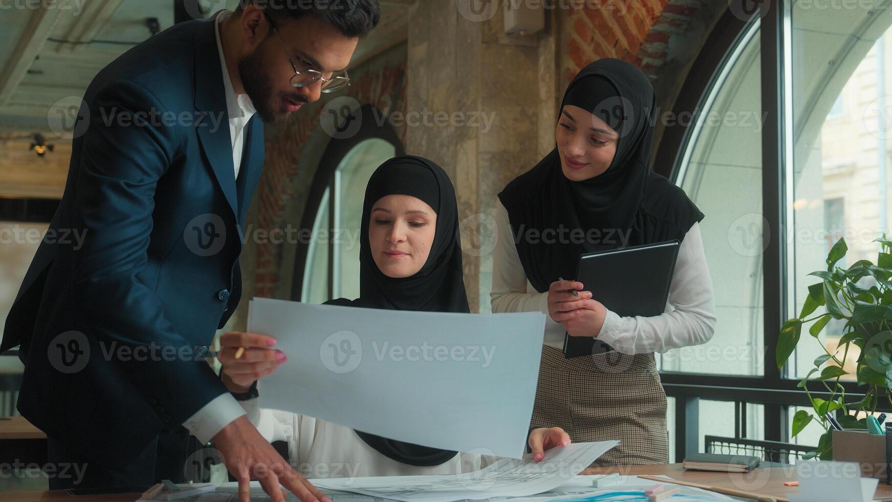 Muslim designer architect in hijab working in office drawing blueprints architecture project on desk business man women multiethnic team colleagues engineers help cooperate discuss building plan draft photo