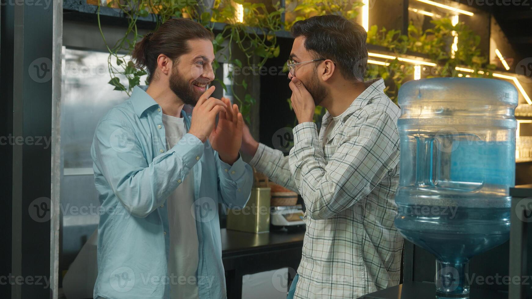 Arabian man drink water cooler in office coffee break pause two business men multiethnic businessmen colleagues coworkers Caucasian Indian guys friends talk secret gossip amazing news shock laughing photo