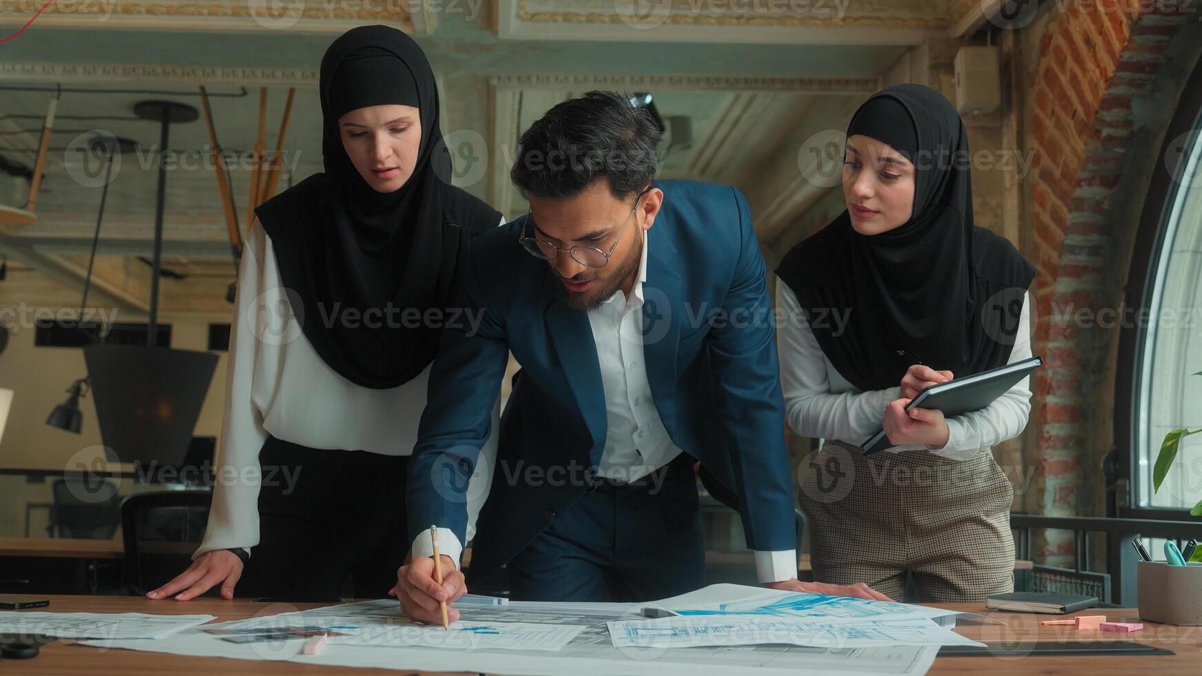 Indian man muslim hijab women business team architects engineers designers builders male female drawing building floor plan construction blueprint sketch on table paperwork planning discuss in office photo