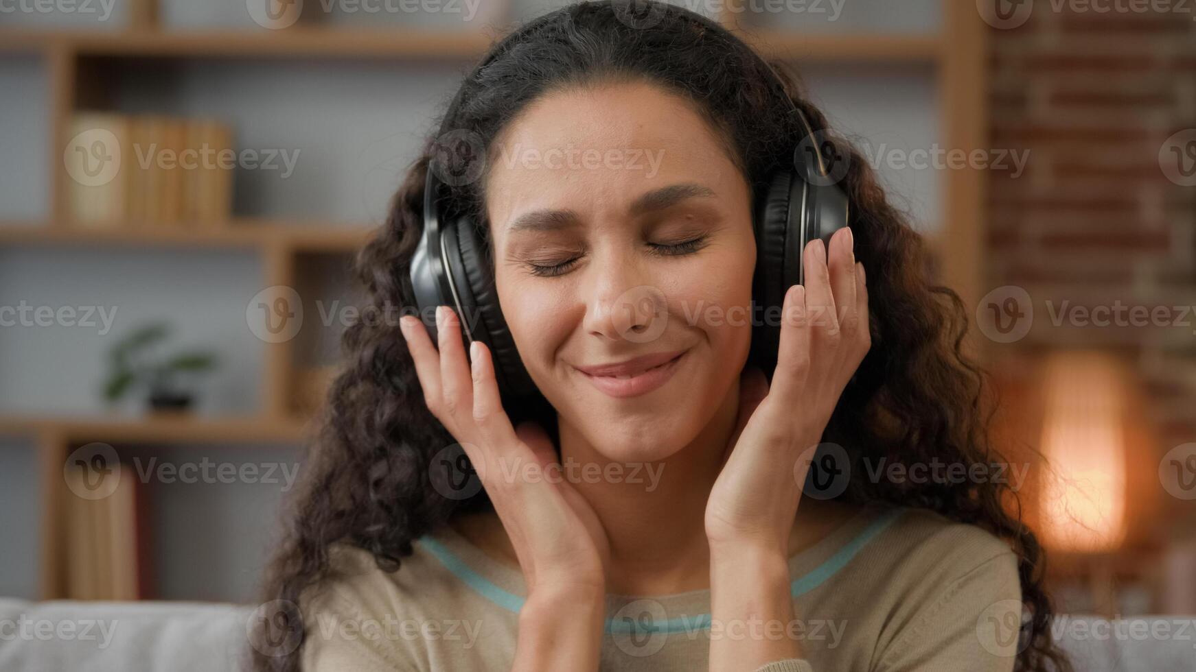 Front view close up smiling Hispanic woman with smiling enjoining lady relaxing at home with closed eyes listening to music in headphones audio sound song feeling well good mood hobby holiday indoors photo
