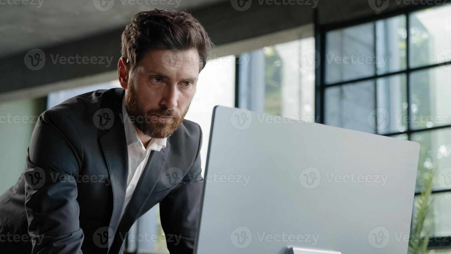 Caucasian busy bearded man adult 40s businessman employer standing in office has problem with paperwork typing data computer online check report contract work with papers and online corporate service photo