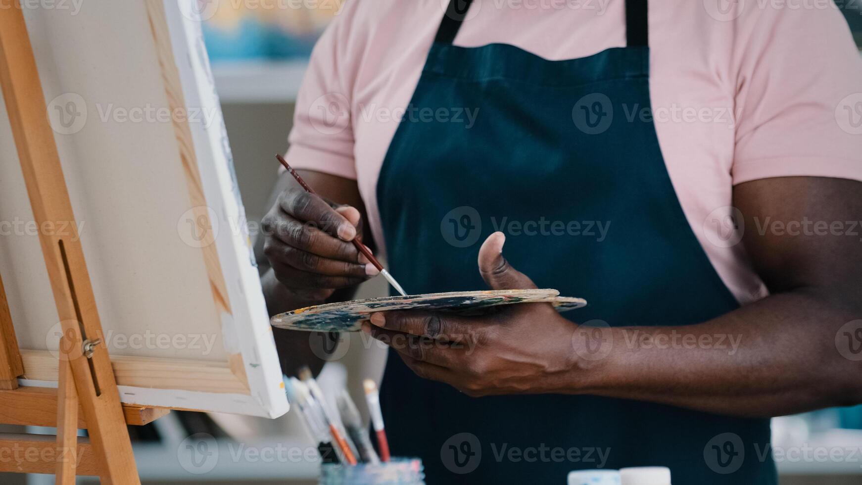 Close-up of male hands unrecognizable African man artist painter holding palette with bright oil acrylic paints colors drawing creates picture on canvas and easel using painting with brushes draw photo