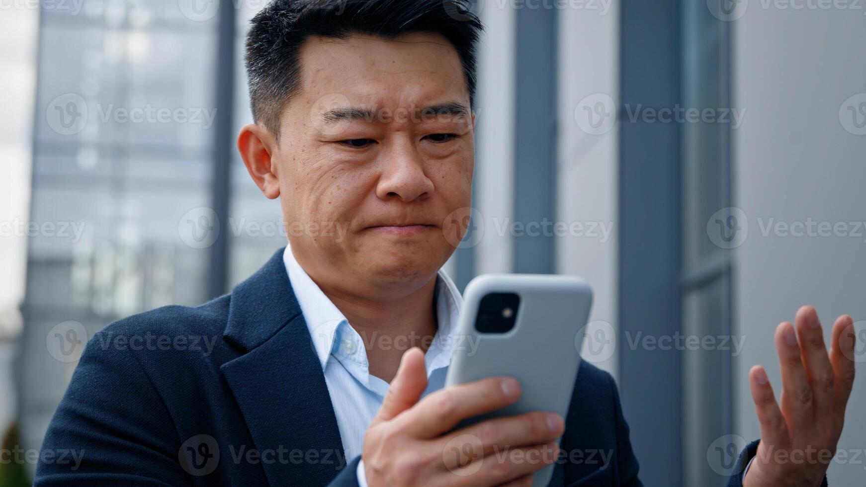 Sad Asian middle-aged adult man mad unhappy businessman feeling annoyed with using broken smart phone low battery problem angry having problem with mobile telephone frustrated bad news outdoors photo