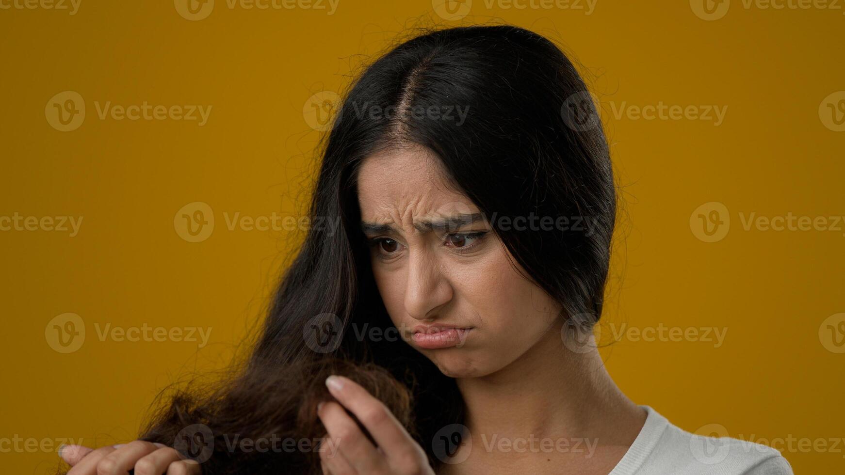 Depressed Indian ethnic woman girl female lady brunette looking at split ends of hairstyle worried feels upset about brittle damaged dry hair loss alopecia hormone problems or vitamins deficiency photo