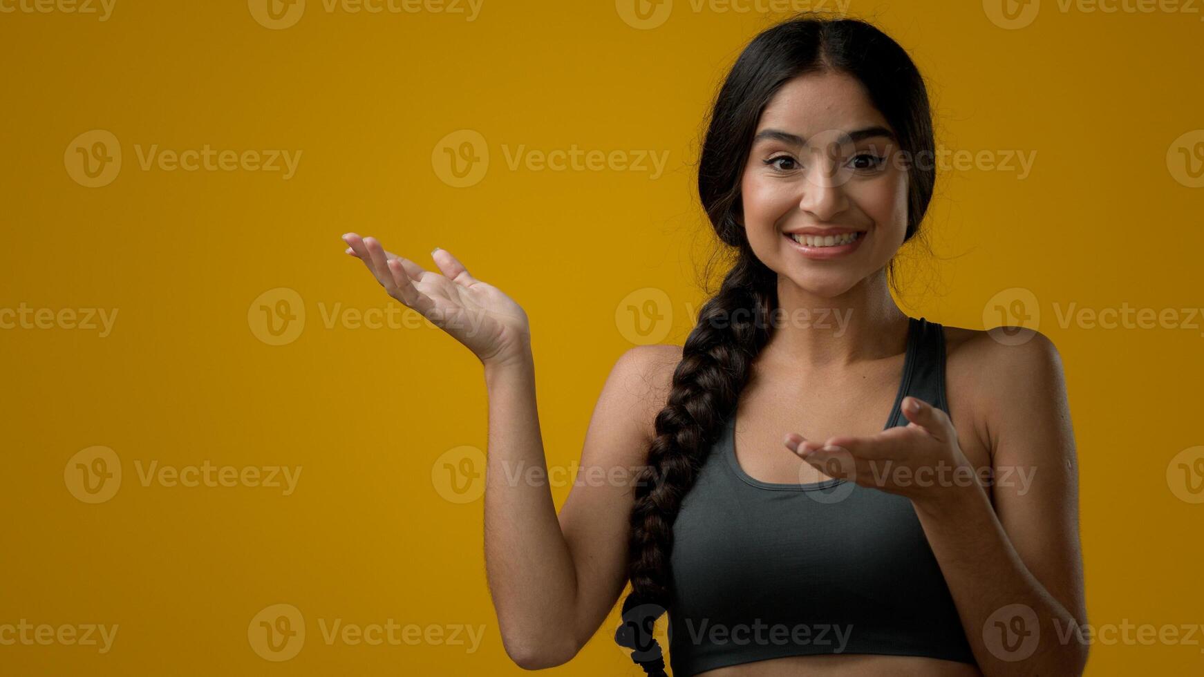 Satisfied Indian woman girl female looking at camera in studio yellow background pointing to side empty copy space advertisement amazement amazing looking to aside astonishment disbelief excited shock photo
