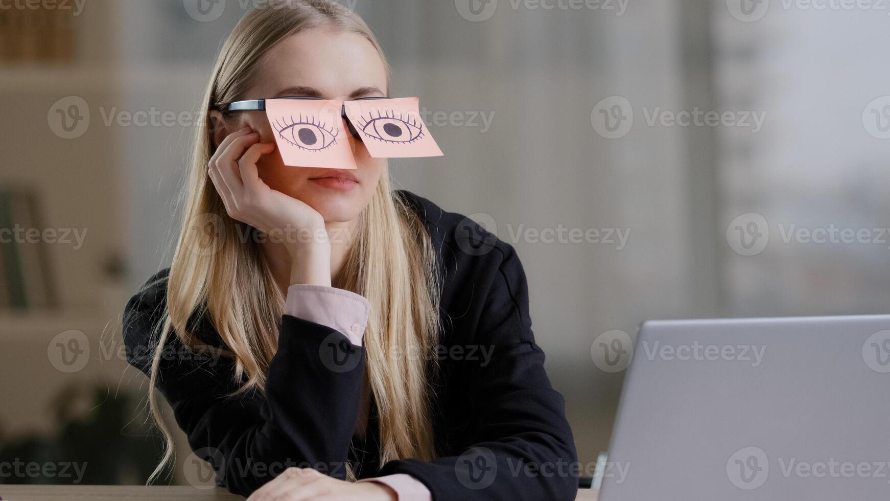 Tired sleepy caucasian woman with adhesive notes on eyes sticky notes on glasses. Lazy exhausted female sit at desk feel bored routine work. Overworked unmotivated lady with stickers on eyeglasses photo