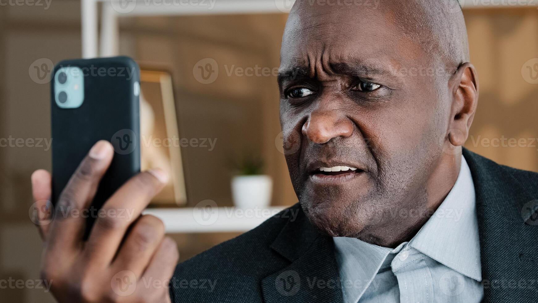 Angry mature elderly African business man having emotionally unpleasant conversation call with smartphone upset failure boss employee bad news shocked reaction disgust despair facial expression photo