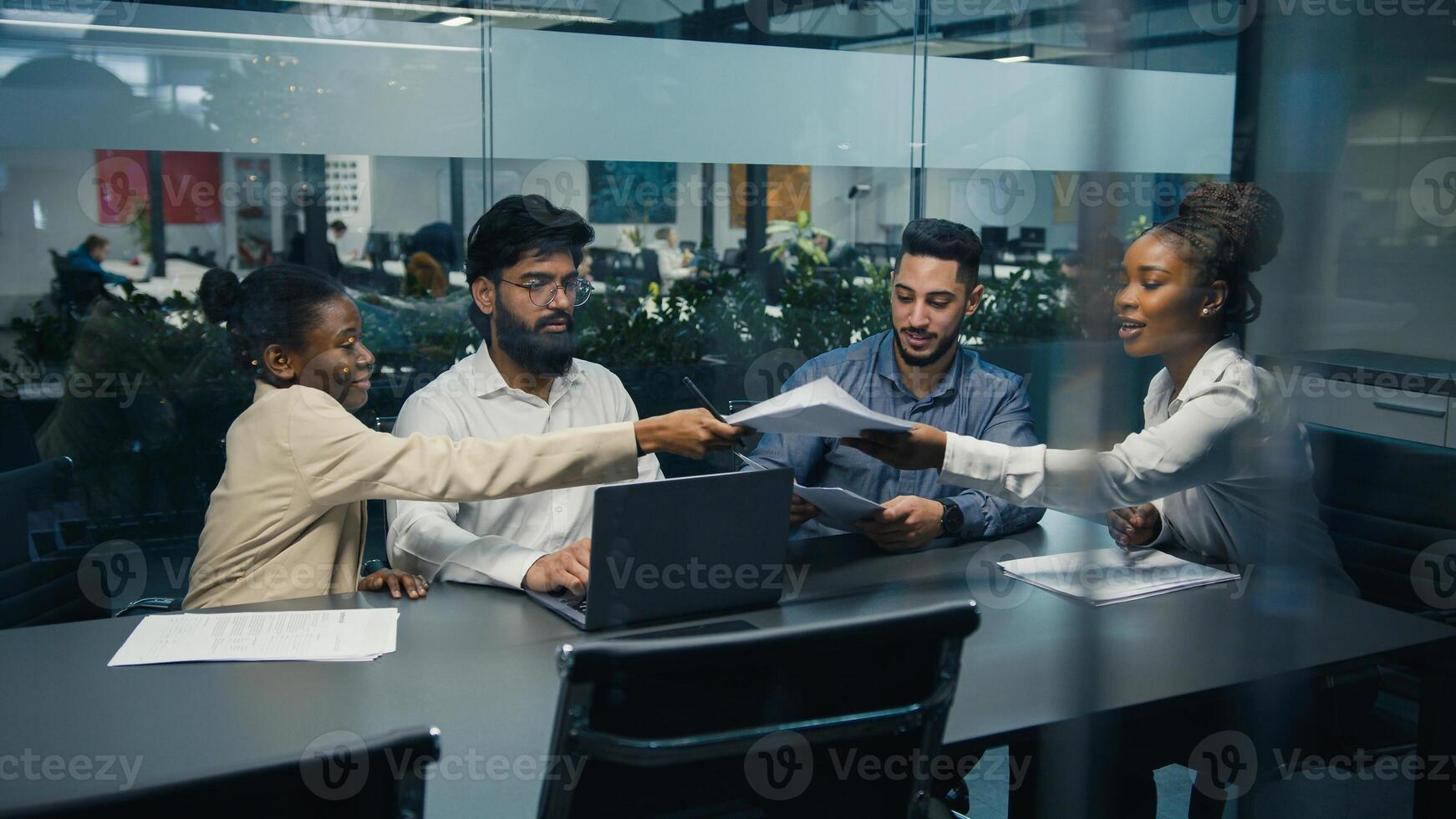 View from behind glass African American female team leader company CEO check strategy with diverse colleagues paperwork documents multiracial business people work project together at office teamwork photo
