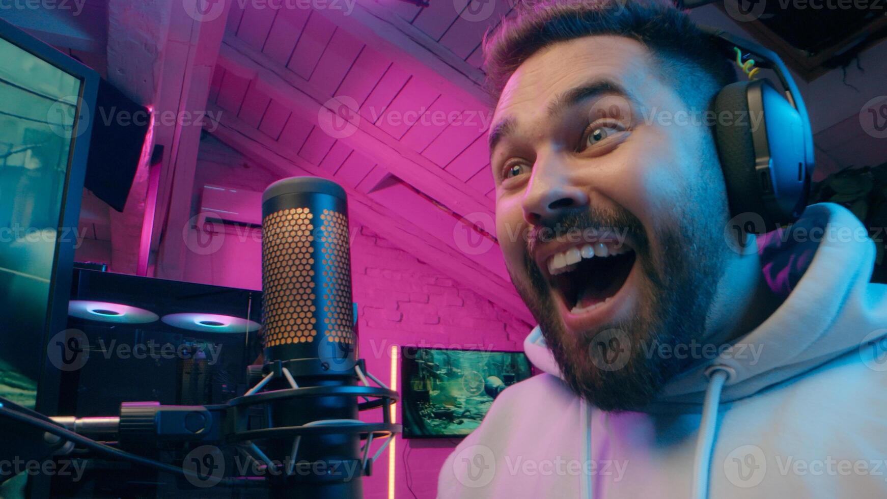 Happy Caucasian male gamer blogger vlog close up talking microphone playing computer gadget game at home e-sport neon guy influencer speak mic host man streaming streamer smile radio gaming vlog photo