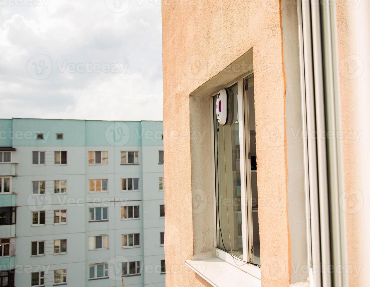 A modern vacuum robot window washer washes glass in an apartment on a balcony. View outside from the street. Safety from falls from a height. photo