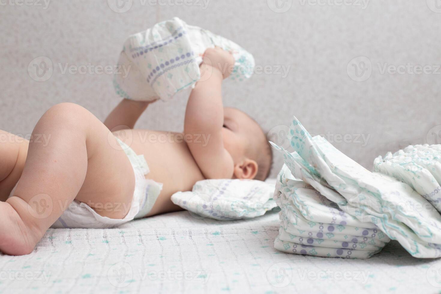 A baby in a diaper lies on a white background plays with a stack of diapers. Copy space for text photo