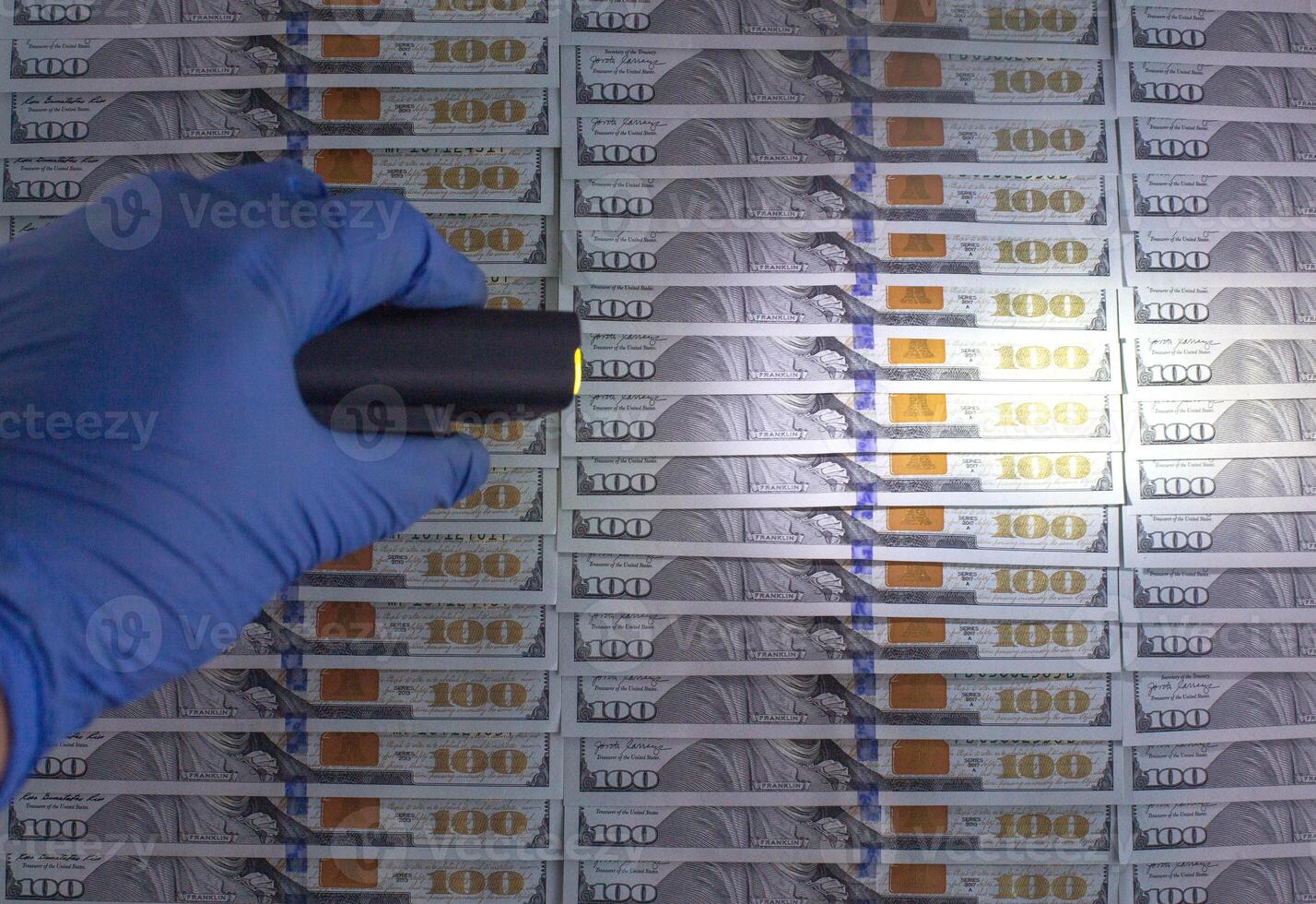 An expert checks American money dollars for counterfeiting with an ultraviolet flashlight. The concept of detention and counterfeiting, copy space for text photo