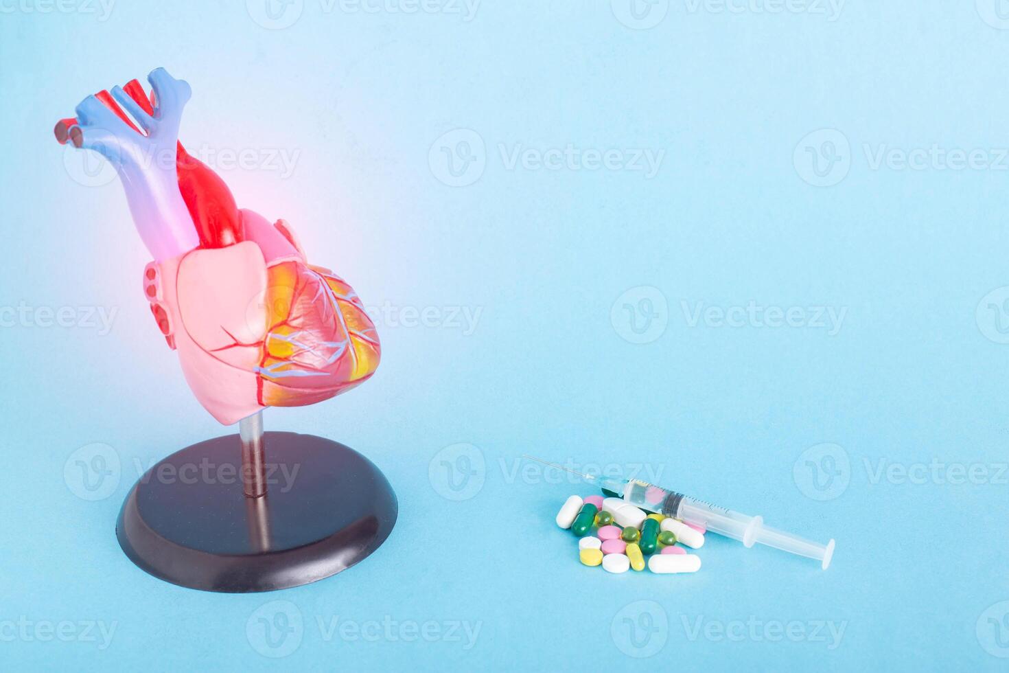 Mock up human heart, pills and syringe on a blue background. Concept of heart disease treatment with medication, pharmacotherapy, copy space for text, stenocardia photo