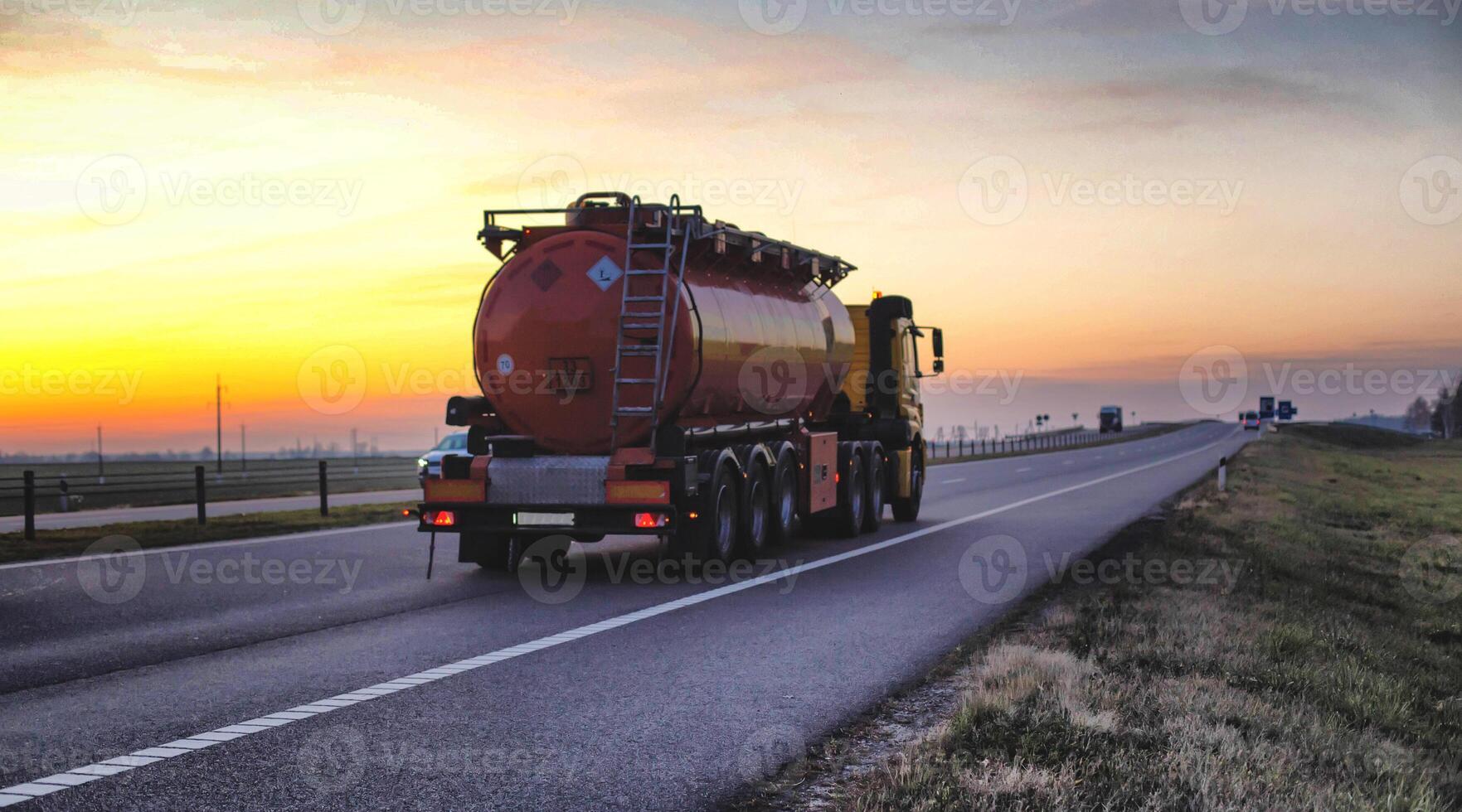 A truck carries a tank of combustible fuel on a highway against a forest and blue sky. The concept of transportation of dangerous goods on the road, license, sunset photo