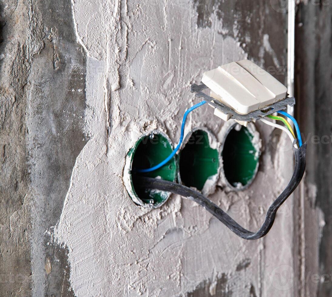 An electric switch hangs on wires from socket boxes built into a concrete wall. The danger of electricity photo