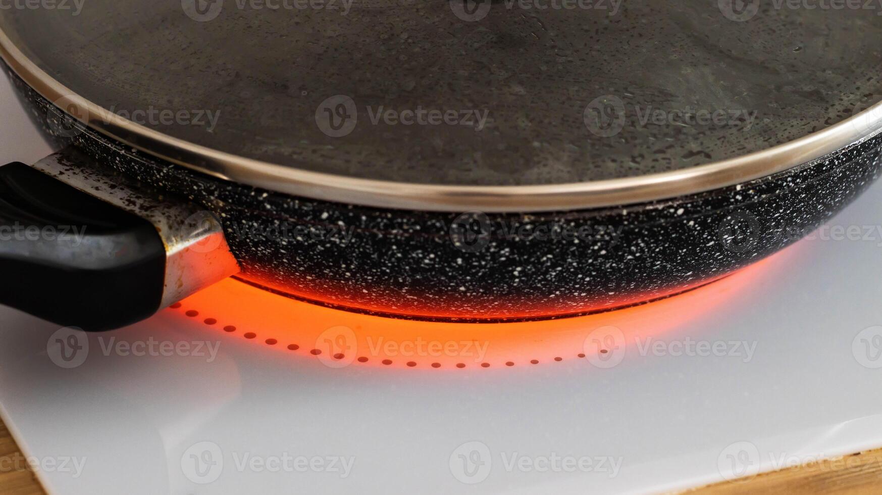 Cooking food in a frying pan on an induction hob, close-up. Modern electric stove in the kitchen. Circle photo
