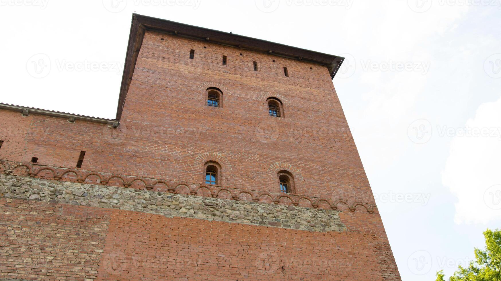 An ancient large castle tower with small red brick windows. Historic building of the 14th century photo