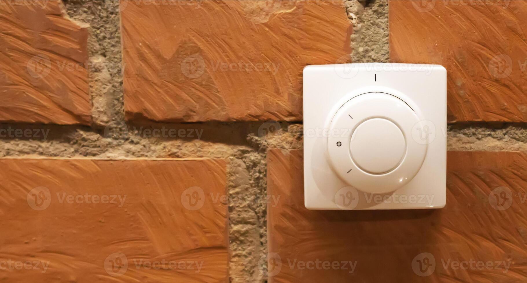Modern white room and floor heating controller on a brick wall, close-up. Adjustment of the comfortable temperature in the room. Copy space for text photo