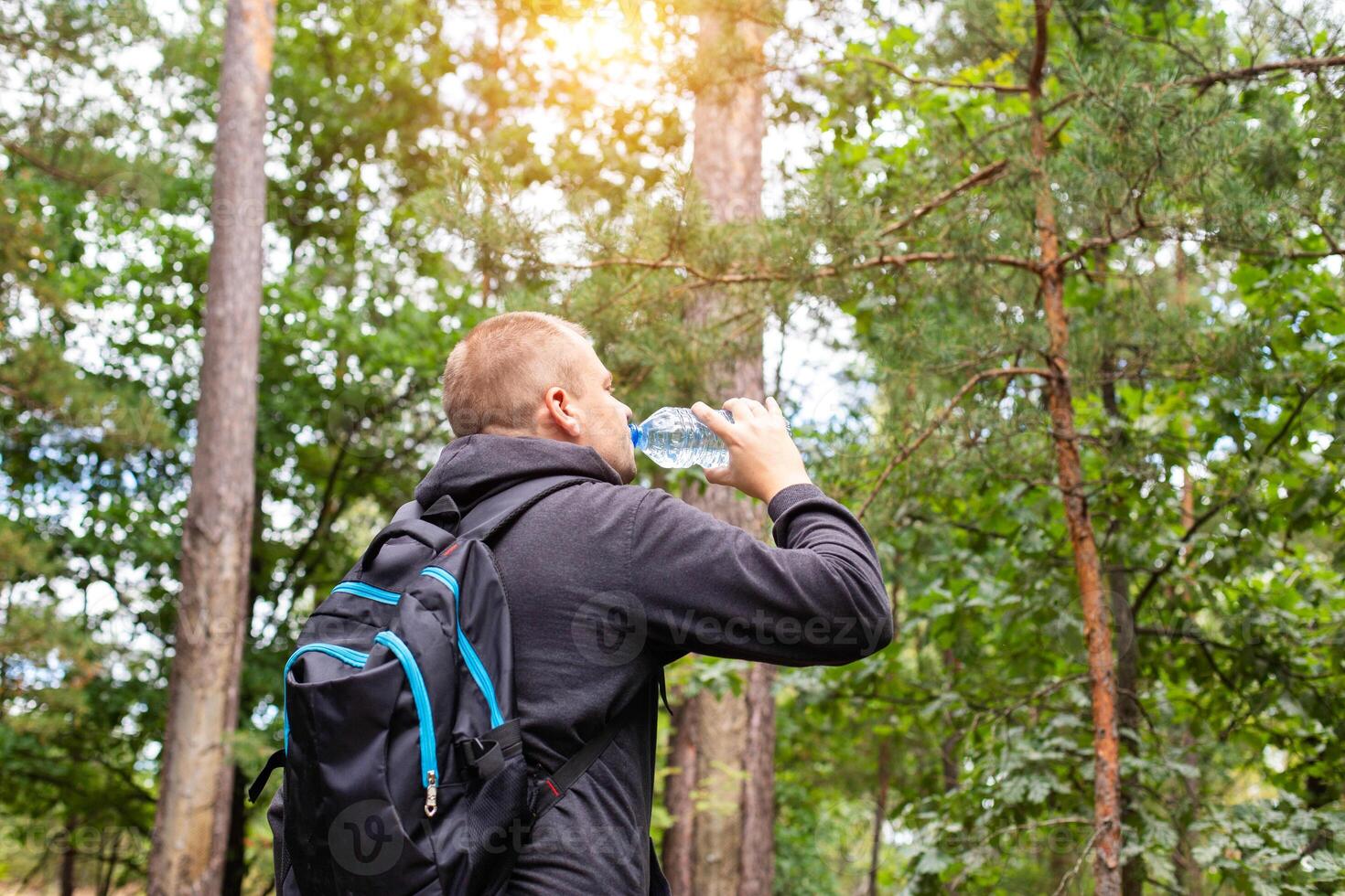 A man drinks water in the forest on a summer sunny day. Survival in the forest, dehydration of the body. photo