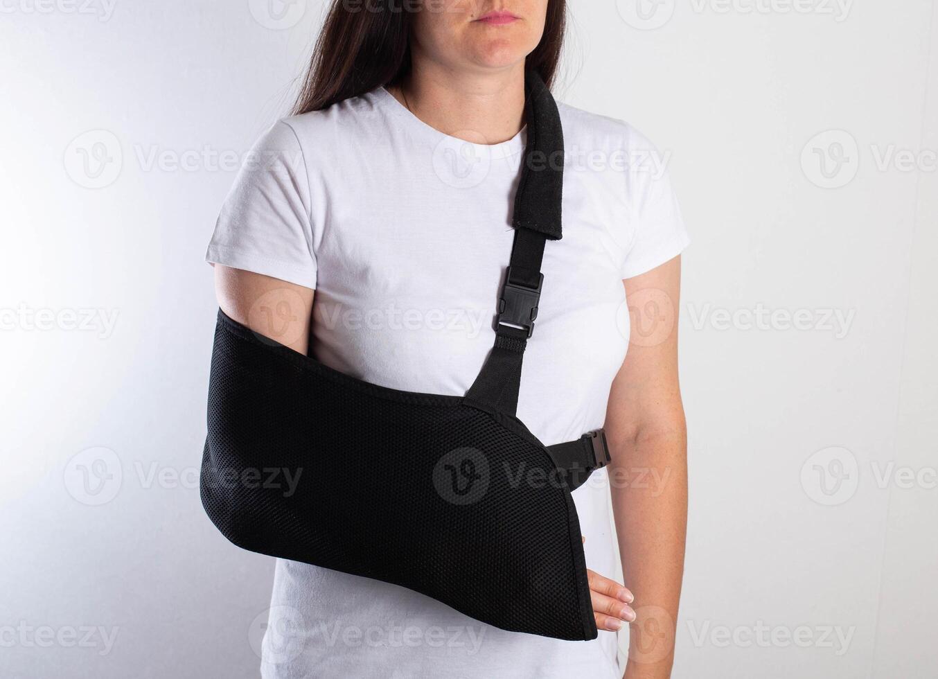 A girl in white with a fixing black bandage on her arm after an injury, a fracture of the radius and a sprain. Arm support bandage, hand immobilization photo