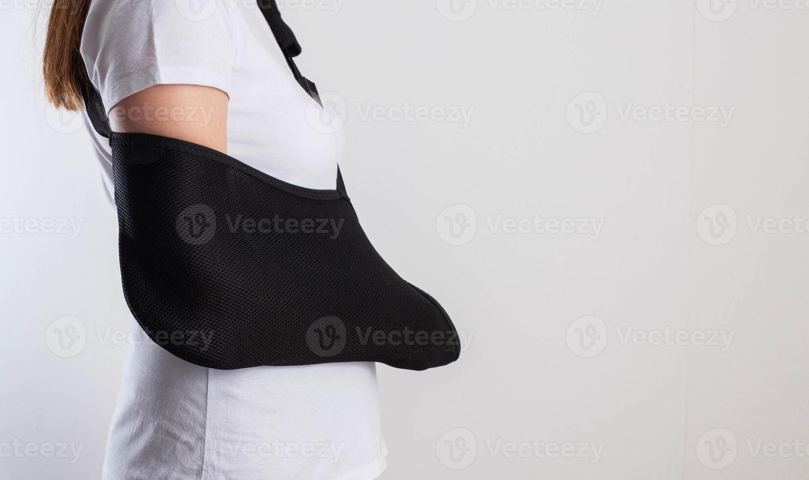 A girl in white with a fixing black bandage on her arm after an injury, a fracture of the radius and a sprain. Arm support bandage, hand immobilization. Copy space for text photo