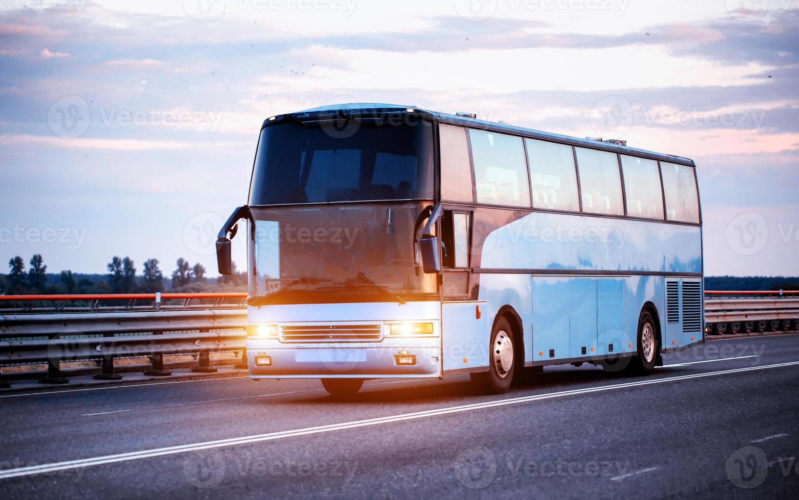 A blue comfortable bus carries passengers along the highway in the evening with the headlights on. The concept of travel and tourist tours from travel agencies. photo
