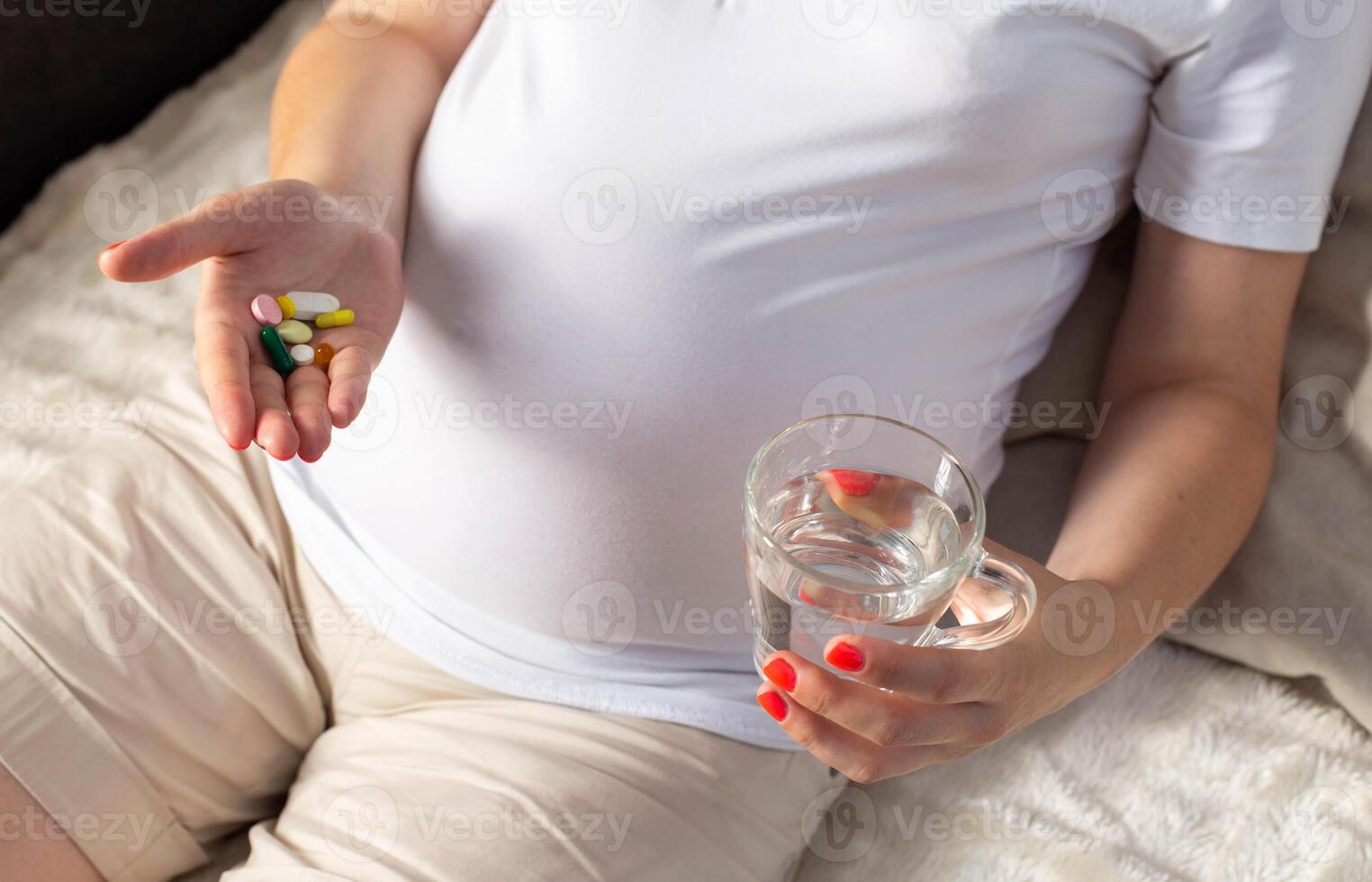 A pregnant girl holds a handful of pills on the palm of her hand. First aid concept for pregnant women. Vitamins and minerals, pain relief during pregnancy, close-up photo