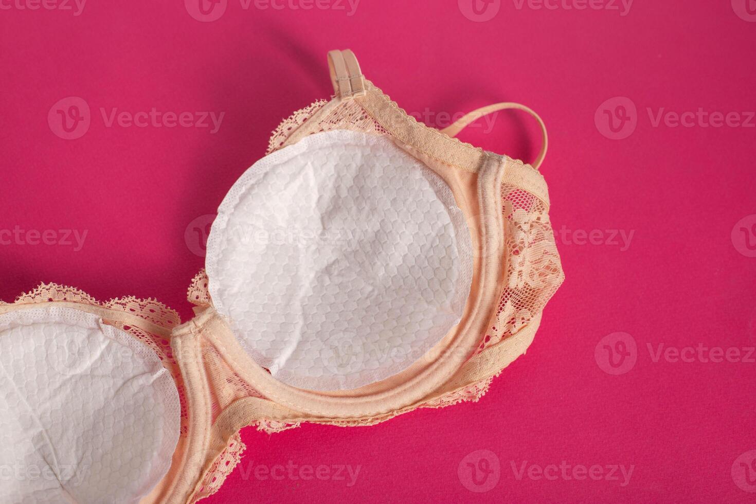 Women's bra with liners against the flow of milk from the breast of a nursing woman on a pink background. photo