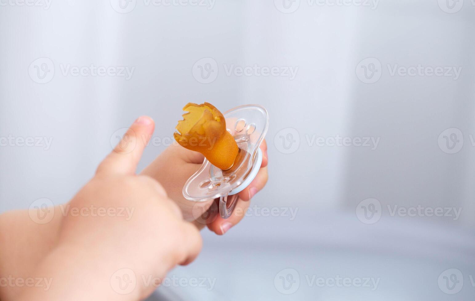 A torn and chewed silicone nipple in the hands of a baby. The concept of problems with bite in children due to the pacifier. Teething, pediatrics. Copy space for text photo
