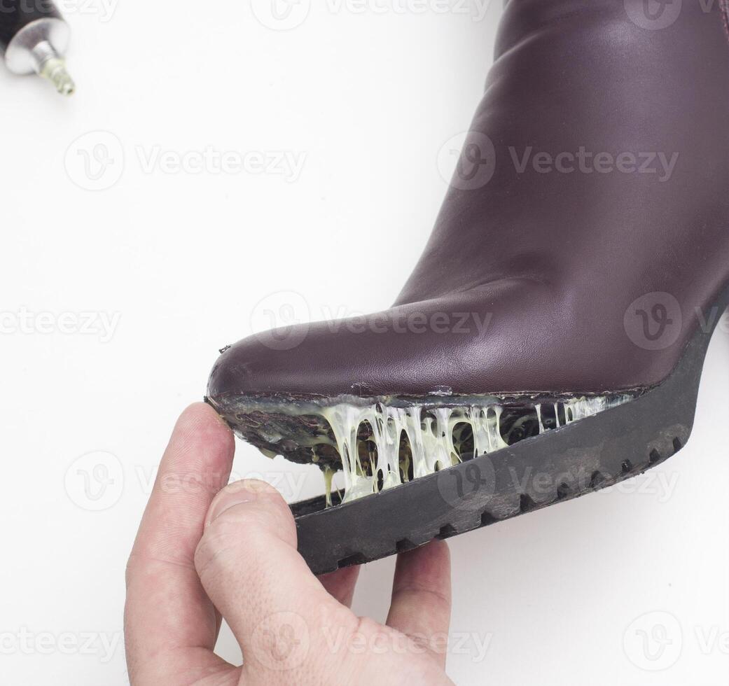 A shoe repairman glues the sole of a women s winter boot. Low-quality shoes concept, boots repair, close-up photo