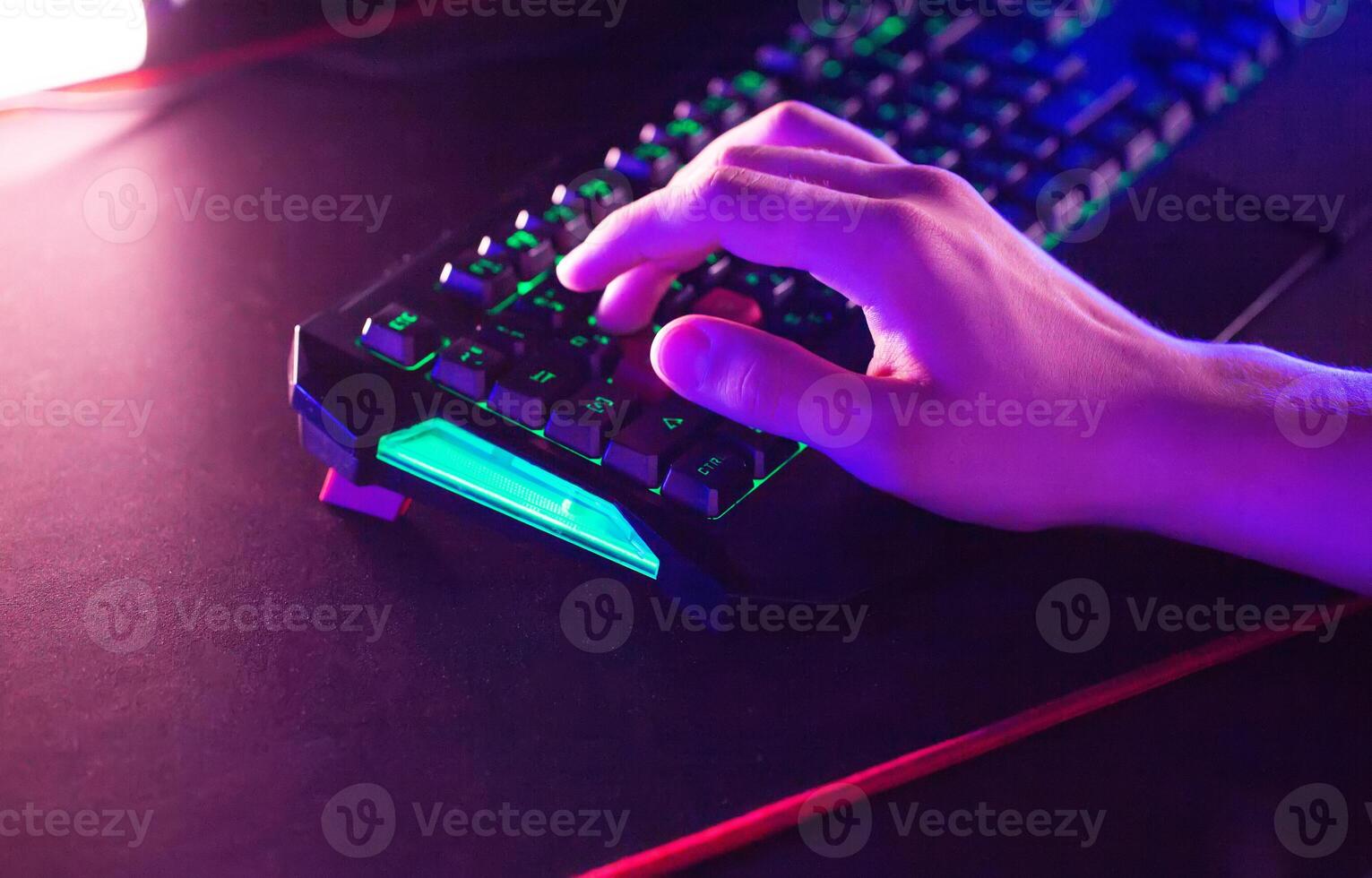 Gamer plays game on PC at computer club, keyboard mouse RGB lightning animation close up. photo