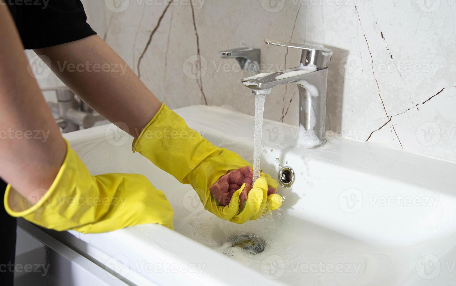 A girl's hands in yellow gloves wash the bathroom sink with a cleaning product for a pleasant smell and shine, close-up. Cleaning company services photo
