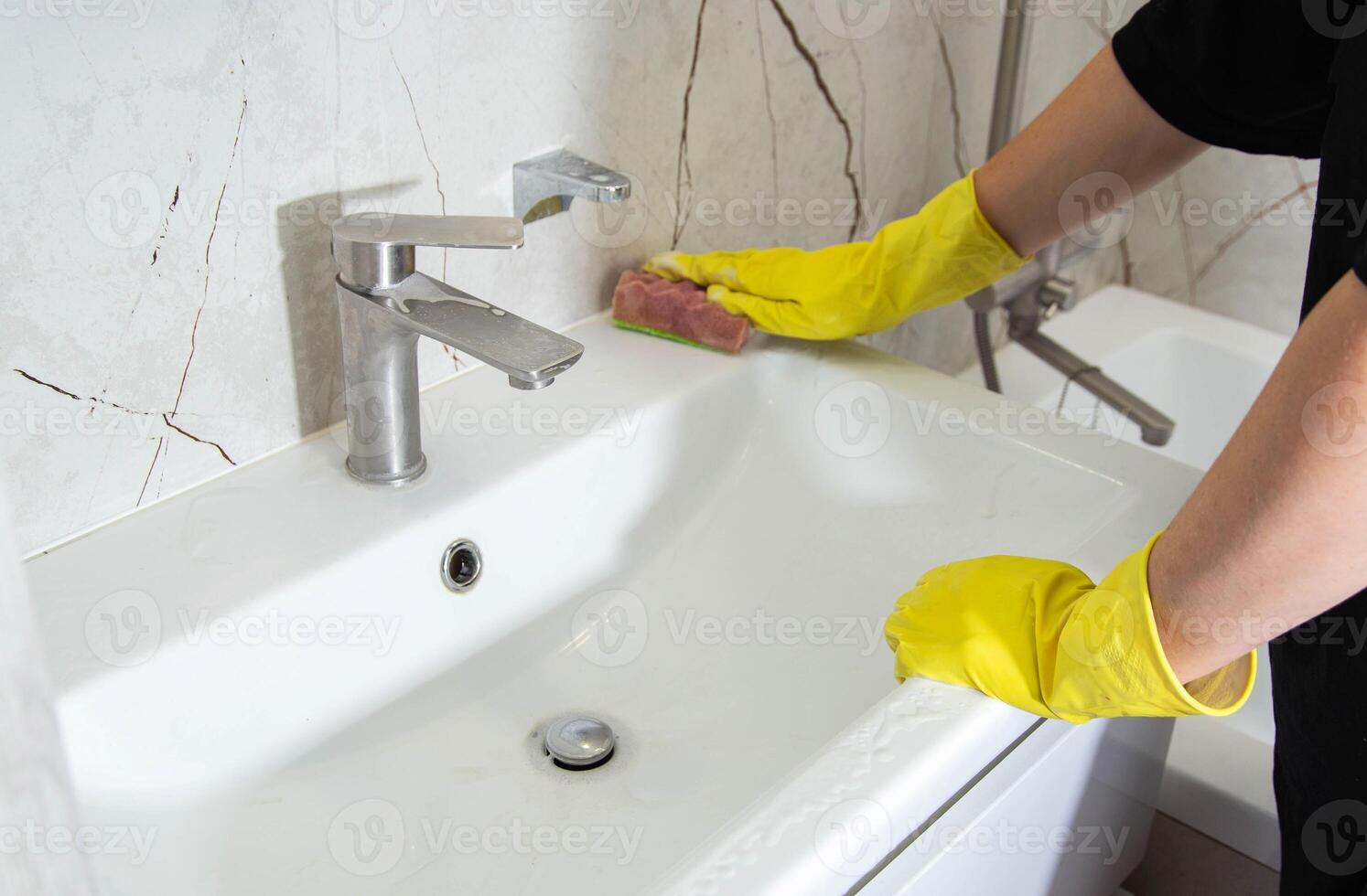 A girl's hands in yellow gloves wash the bathroom sink with a cleaning product for a pleasant smell and shine, close-up. Cleaning company services photo