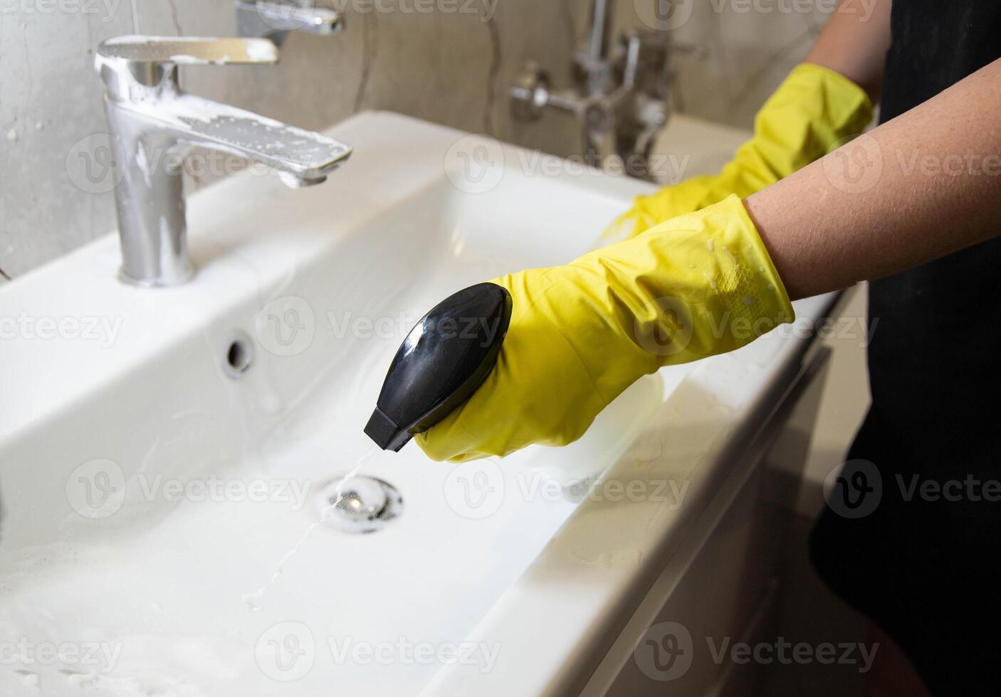 A girl washes and cleans the sink with a cleaning agent wearing yellow rubber gloves. Whitening and shine product, close-up. Copy space for text photo