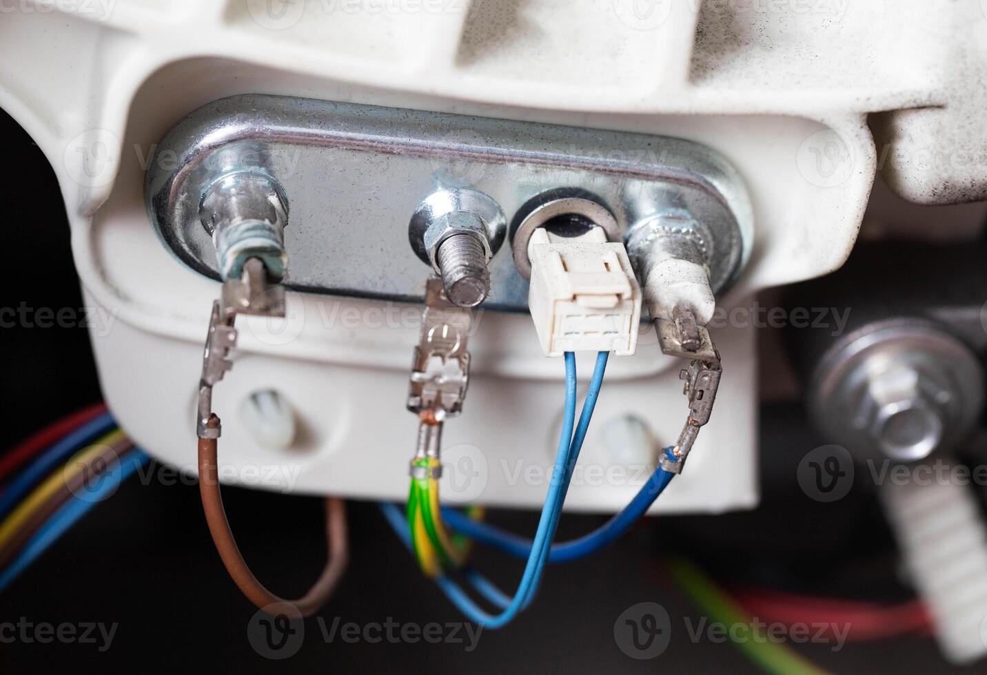 An electric heating element with a thermostat is connected with electrical chips. Repair and replacement of temperature sensor and heating element, hard water, close-up photo