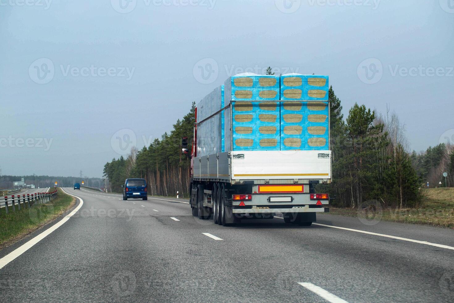 A truck with a semi-trailer transports a bulk load of insulation for construction along a country road in the spring. Copy space for text, industry photo