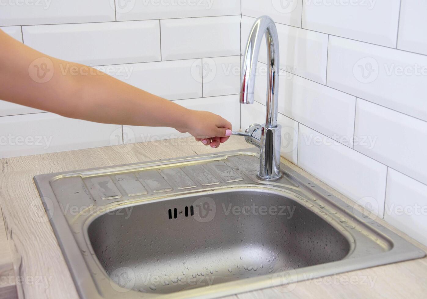 The girl's hand is holding on to the water tap from which water does not flow in the kitchen. Concept of shutting down the water supply on schedule for repairs. Copy space for text photo