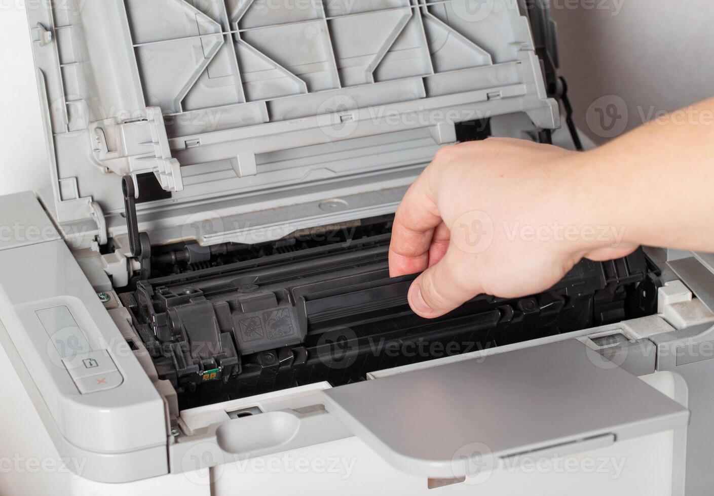 A man takes out a cartridge from a laser printer for maintenance and refilling toner, close-up photo